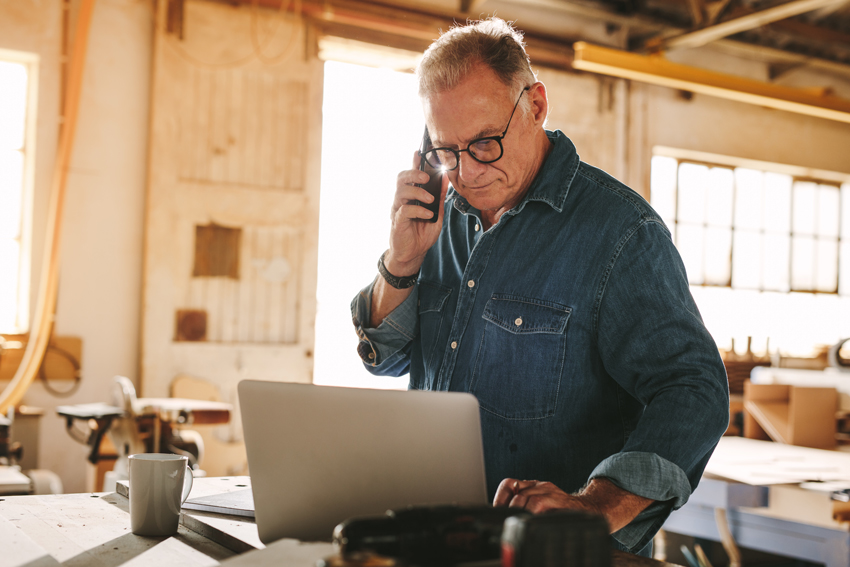 man holding a phone to his ear and looking at a laptop